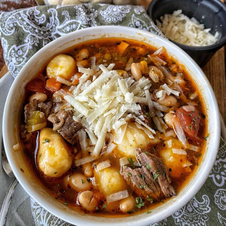 A bowl of beefy dumpling soup topped with shredded cheese