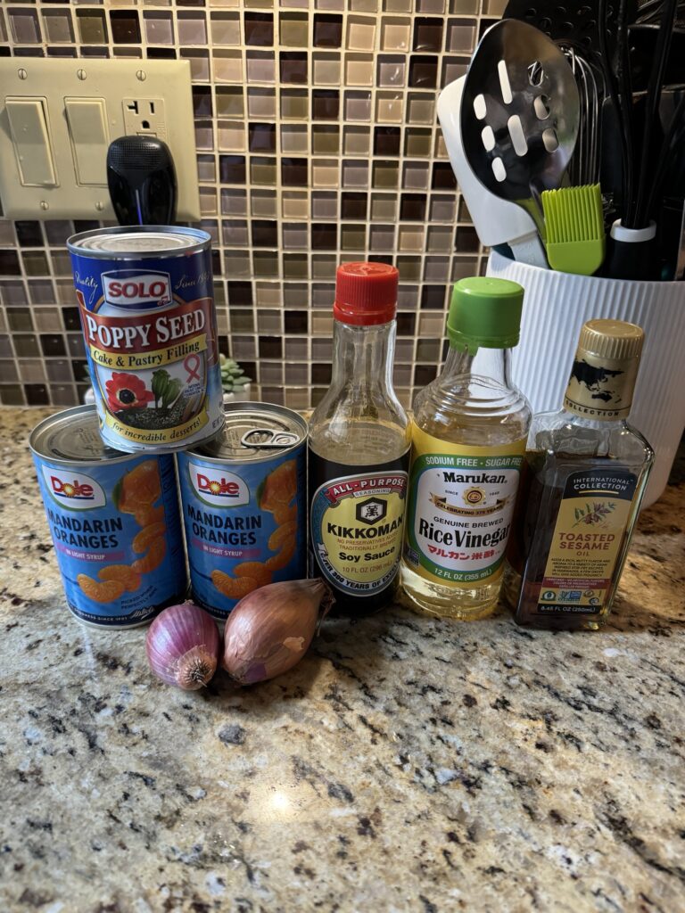 The ingredients for the salad, including cans of Mandarin oranges, a can of poppy seed filling, soy sauce, rice vinegar, and toasted sesame oil