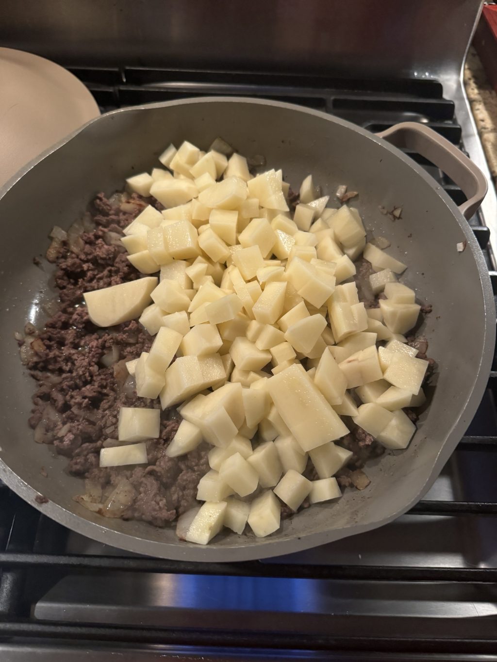 Cut up potatoes and ground beef cooking in a pan