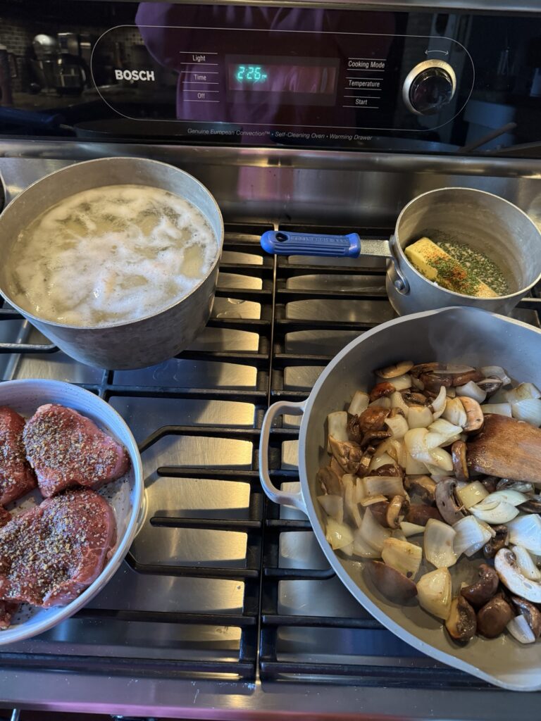 The steak, potatoes, butter, onions, and mushrooms all cooking up on the stove top