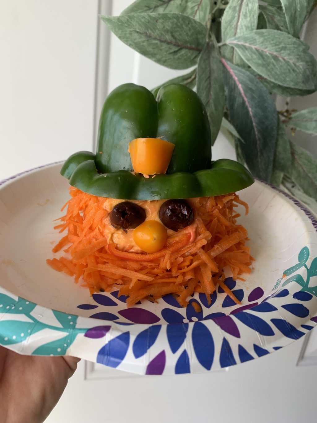 A cheeseball in the shape of a leprechaun with olive eyes, carrot beard, and green pepper hat.