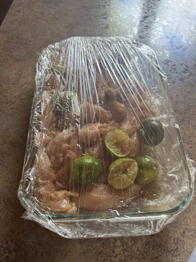 Marinated chicken in a baking dish covered with saran wrap