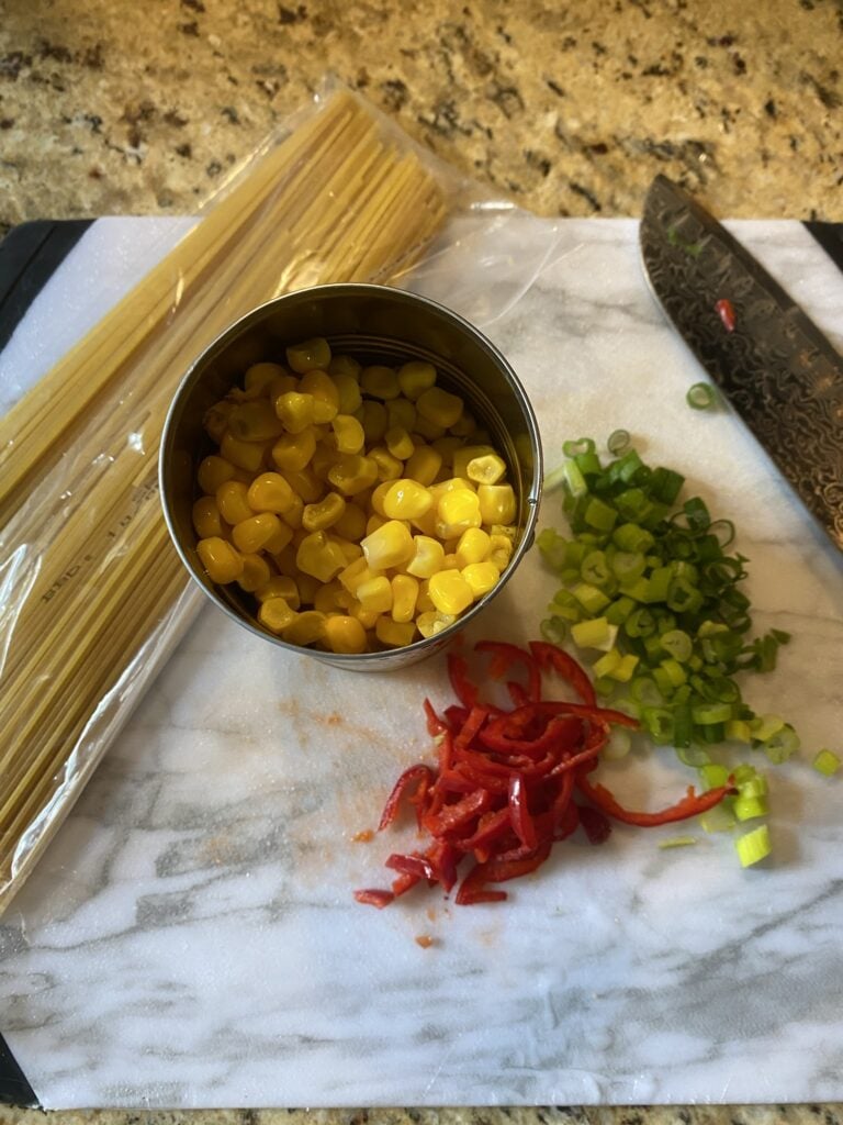 A can of corn, chopped garnish, and uncooked spaghetti