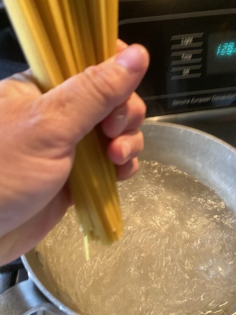 Uncooked spaghetti held over a boiling pot
