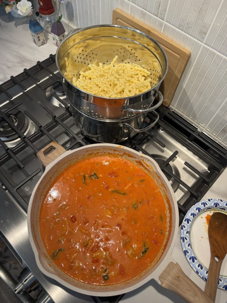 A strainer with pasta next to a bowl of tomato sauce