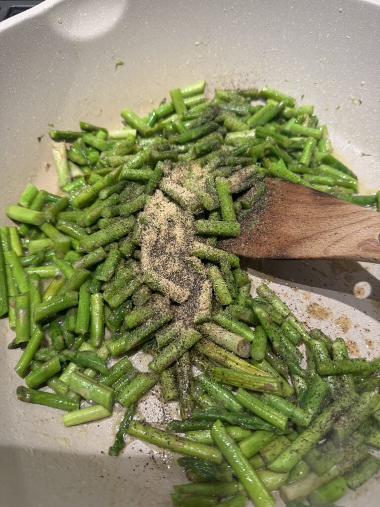 Chopped asparagus topped with seasonings in the pan