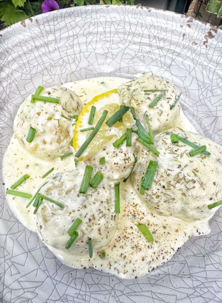 A bowl of the meatballs topped with green onion and lemon