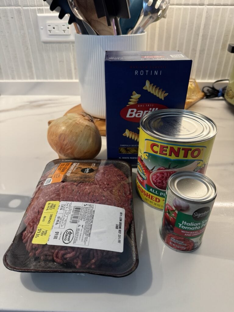 The meat sauce ingredients, including canned tomatoes, onion, and boxed pasta