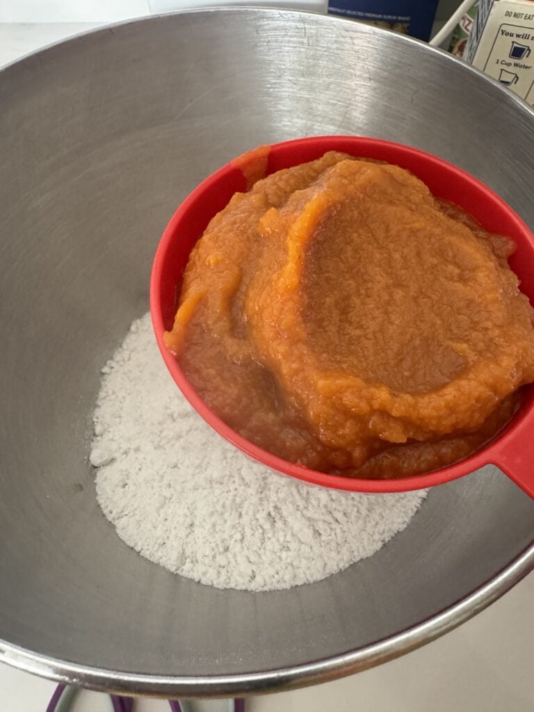 Pumpkin pie mix in a red spoon over the dry cake mix in a metal bowl