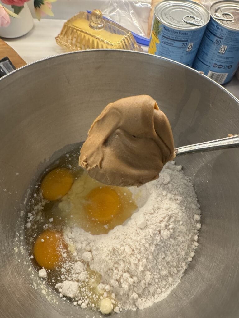 A big spoon of peanut butter over eggs and cake mix in a bowl