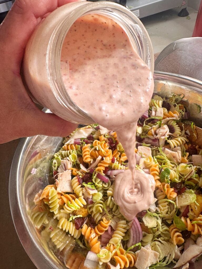 Cranberry dressing being poured over the pasta salad