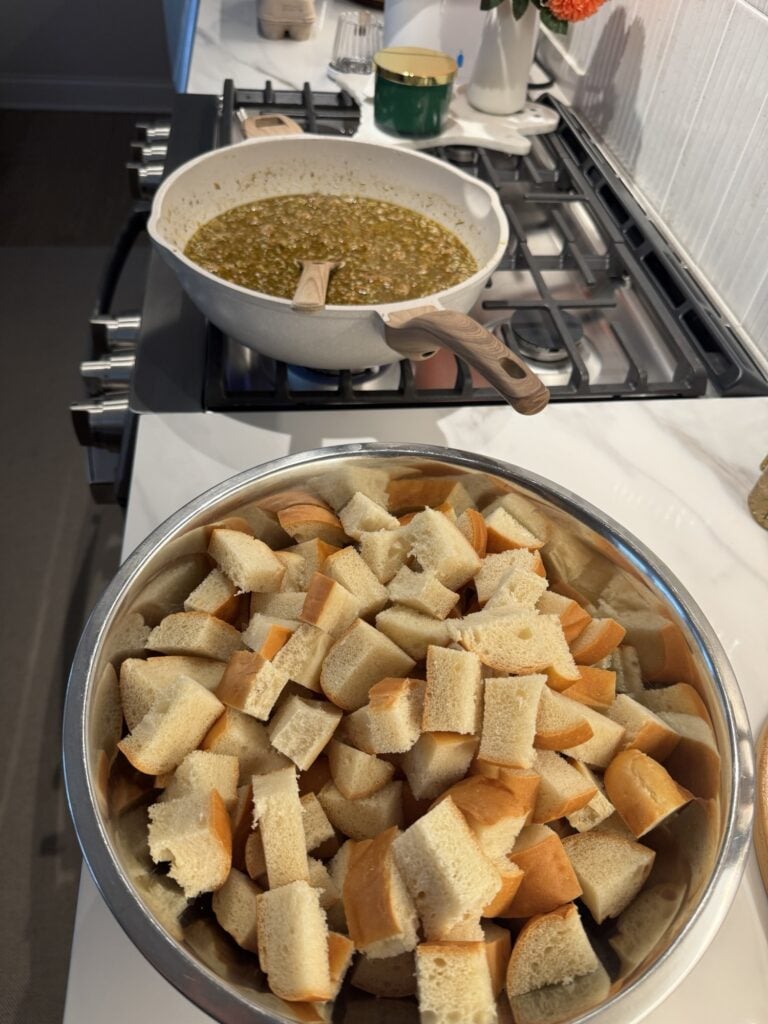 Gravy in a pan on the stove behind French bread cubes on the counter
