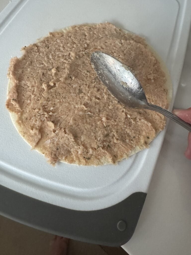 The chicken mixture being spread on the tortilla with a spoon