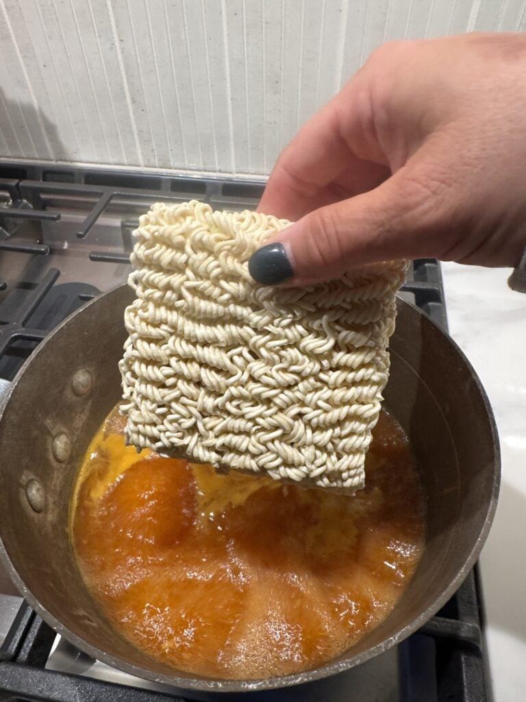 A block of instant ramen noodles held over broth