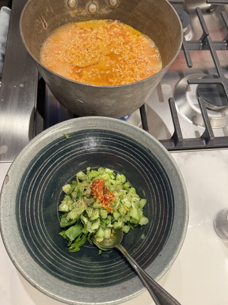 The bowl with the veggies and chili crunch next to a big pot of broth