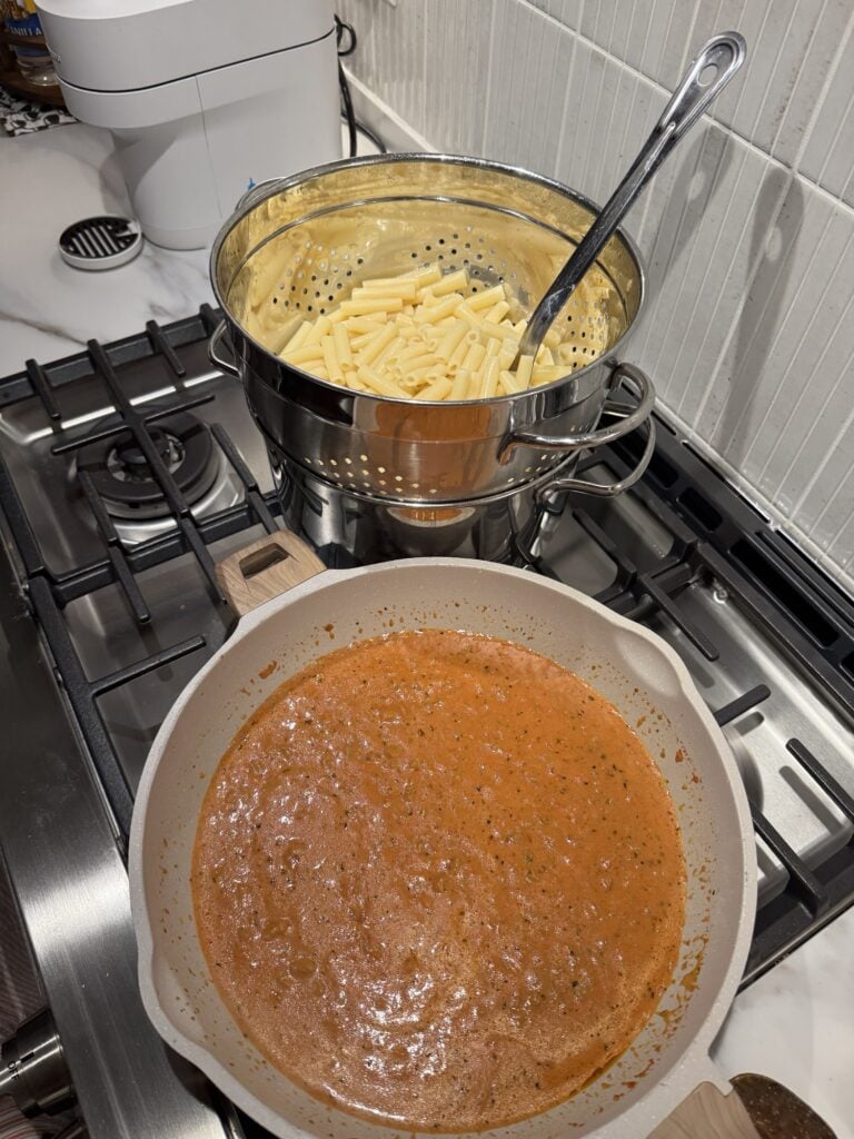 Pasta sauce in a pot with a pot of noodles behind it