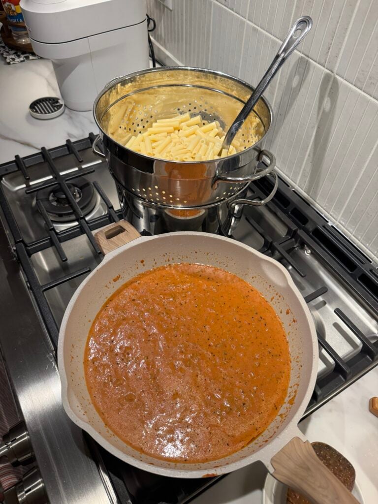 Pasta sauce in a pot with a pot of noodles behind it