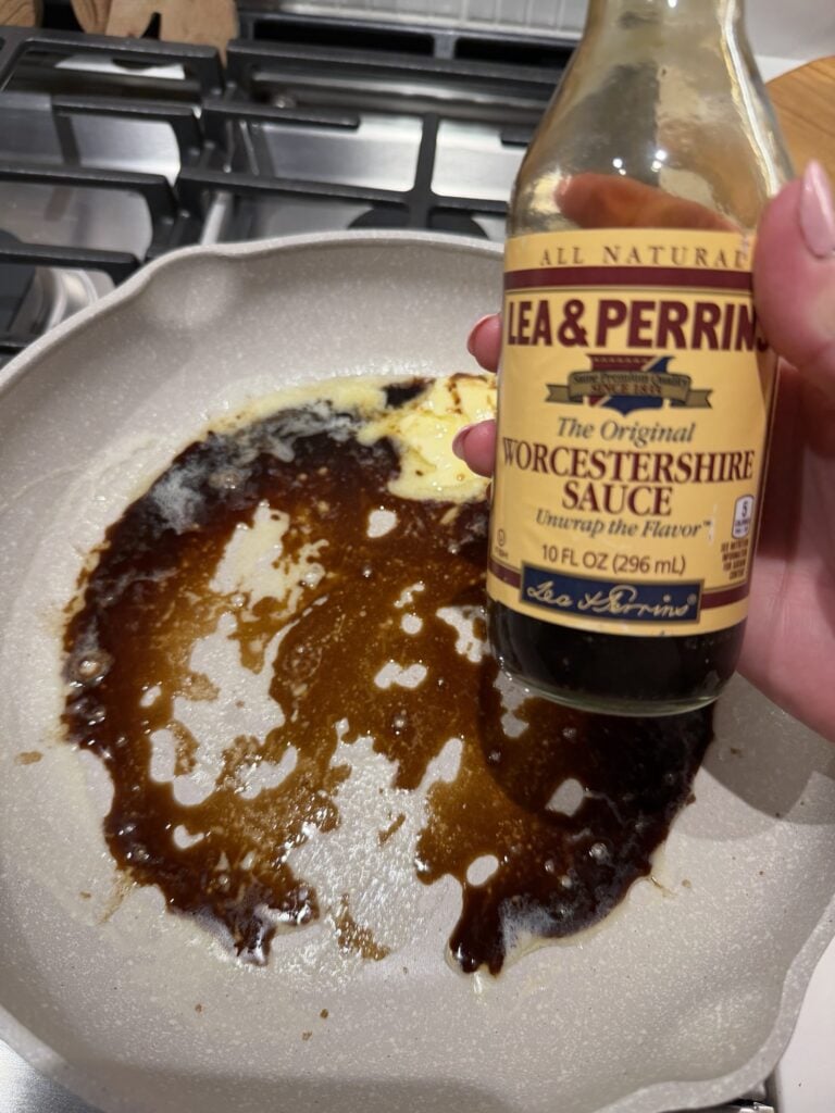 A bottle of Worcestershire sauce over a pan sizzling with the sauce and butter