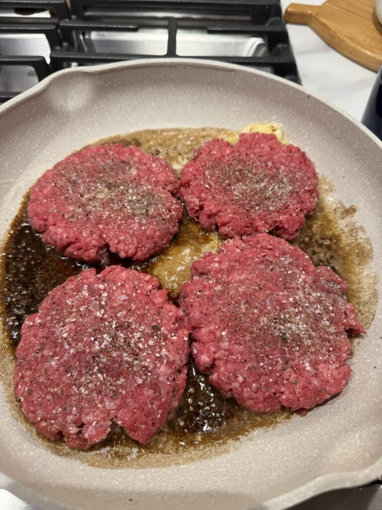 Seasoned burger patties sizzling in the pan