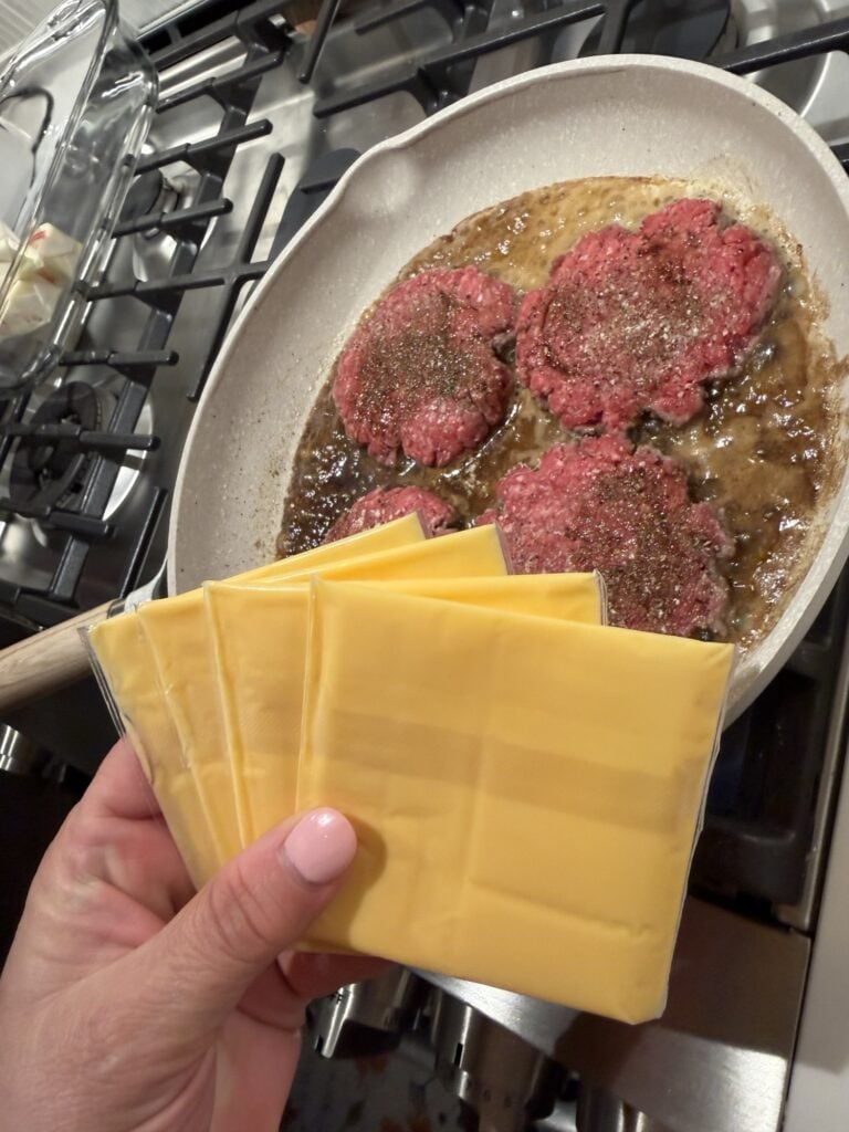 Slices of American cheese held over the sizzling burgers