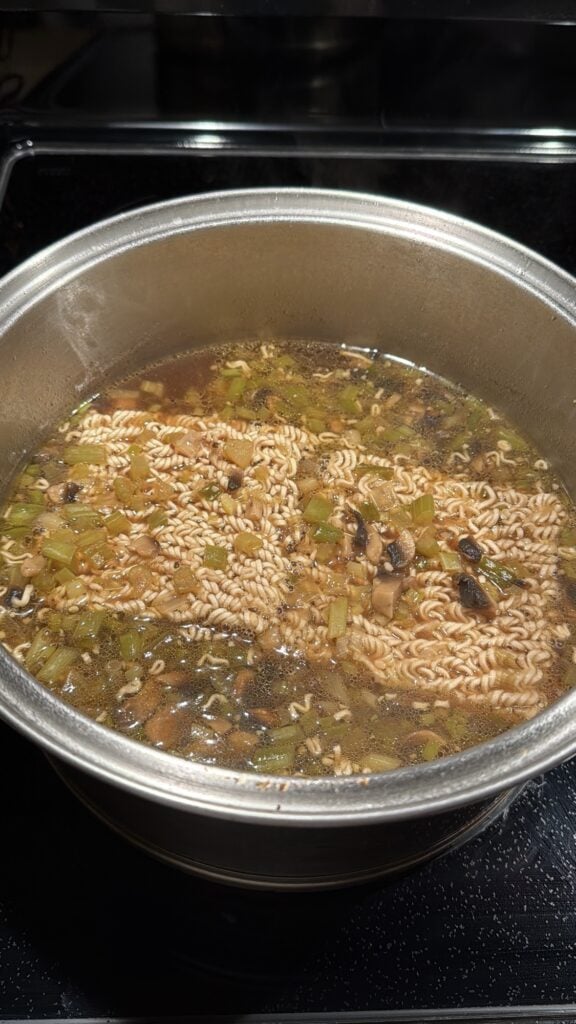 The soup, with blocks of ramen noodles, simmering on the stove