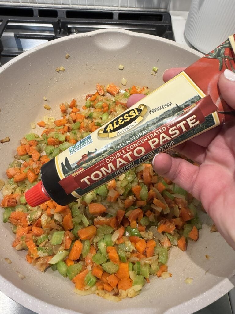 A tube of tomato paste over diced veggies in the pan