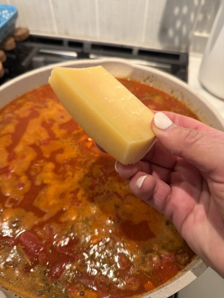 A piece of Parmesan rind held over the simmering soup