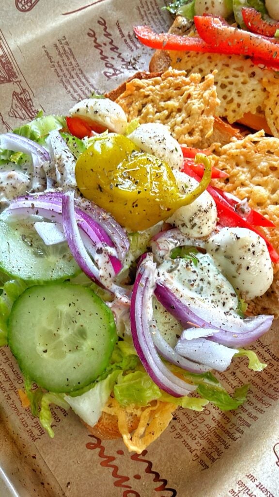 A close up of the sandwich ingredients, including red onion, cucumbers, cheese, and pepper