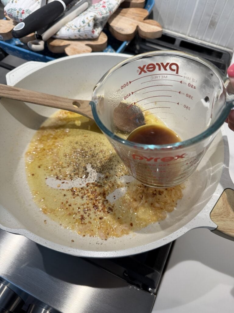 Worcestershire sauce in a measuring cup over sizzling seasoned butter in the pan