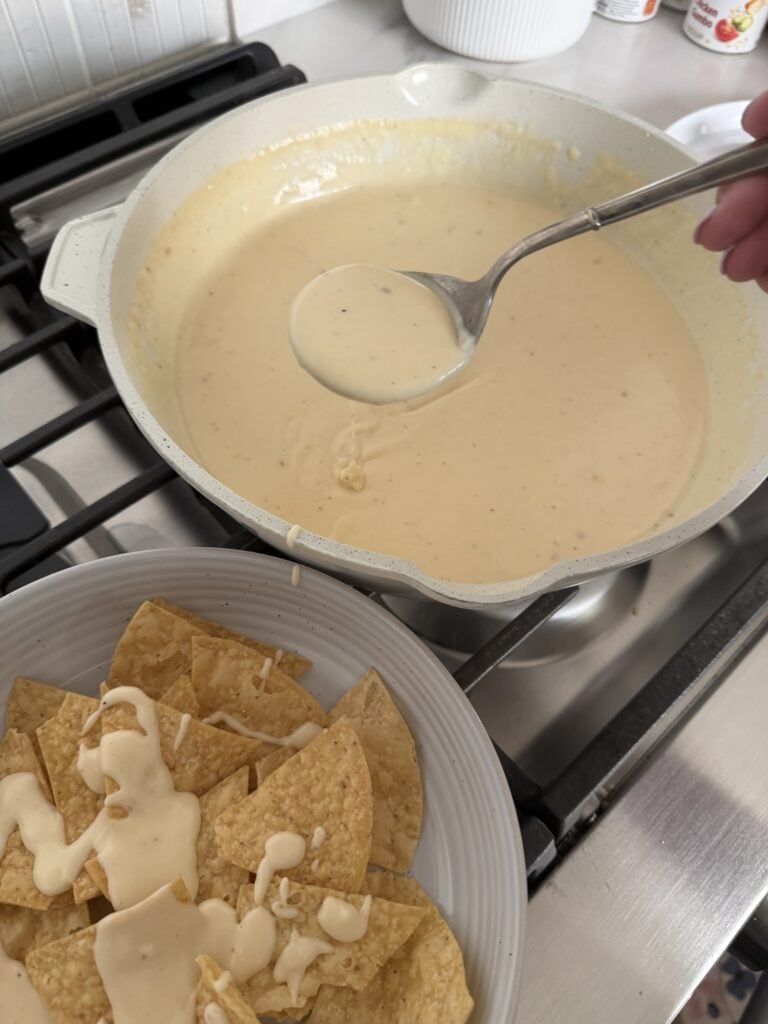 Cheese sauce being spooned over tortilla chips