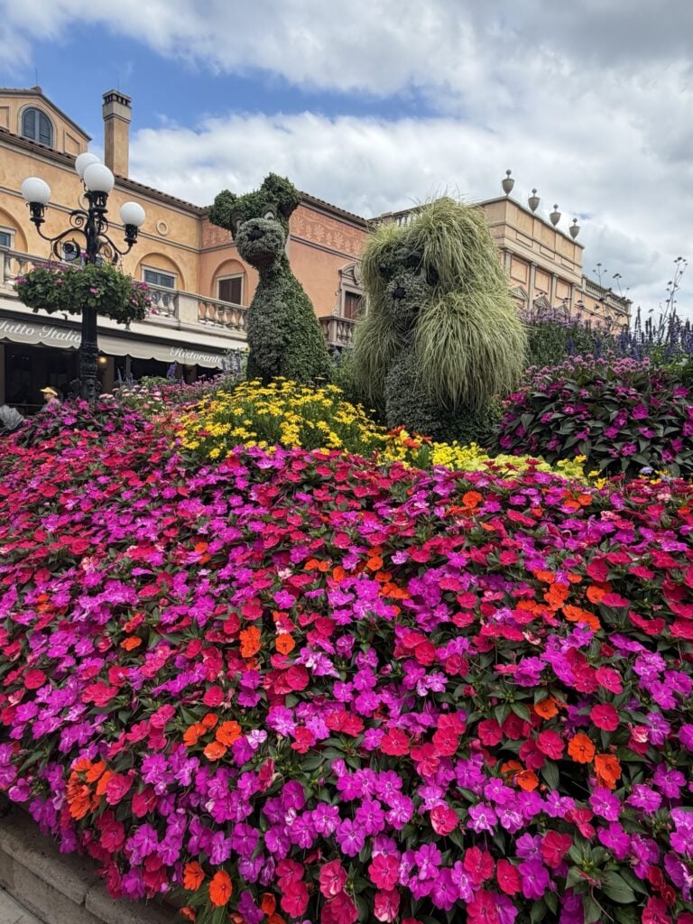 Flowers of different colors surrounding hedge sculptures of Lady and the Tramp