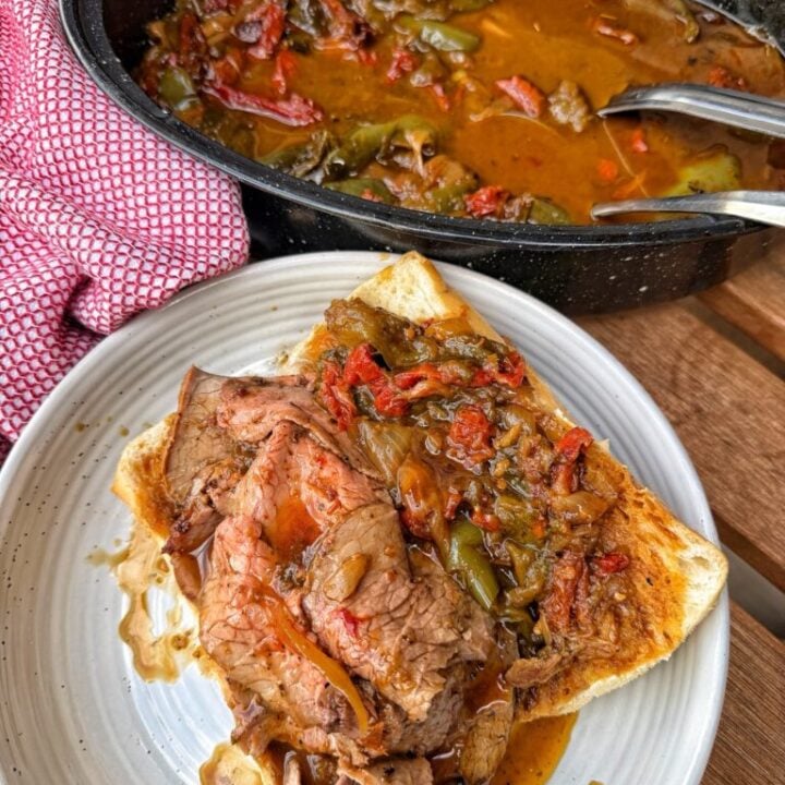 An open Italian Beef Sandwich on a plate in front of a slow cooker with more Italian Beef