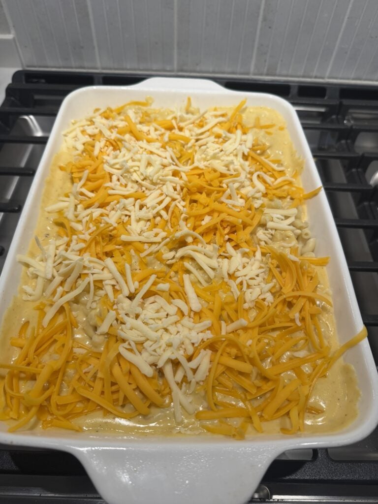 The macaroni in baking dish covered in cheese sauce and shredded cheese before being baked
