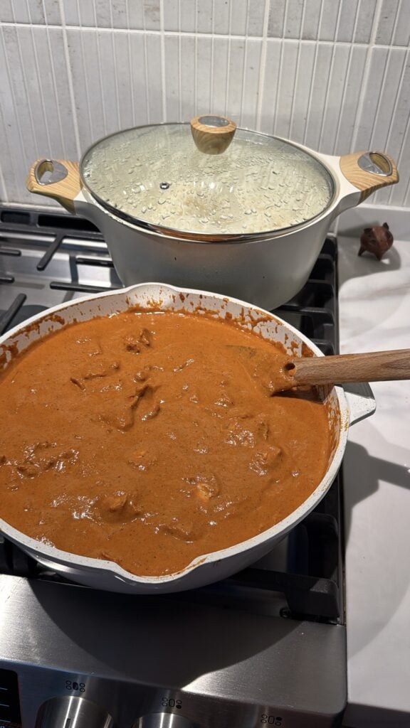 The butter chicken in a pan in front of a pot of rice