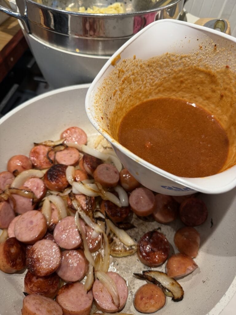 Sausage slices and onions in the pan, the sauce about to be poured over them