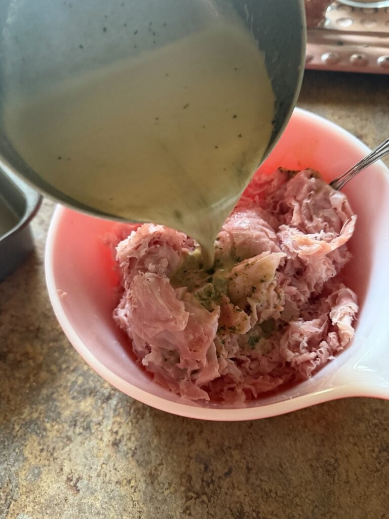 The creamy sauce being poured over the ham