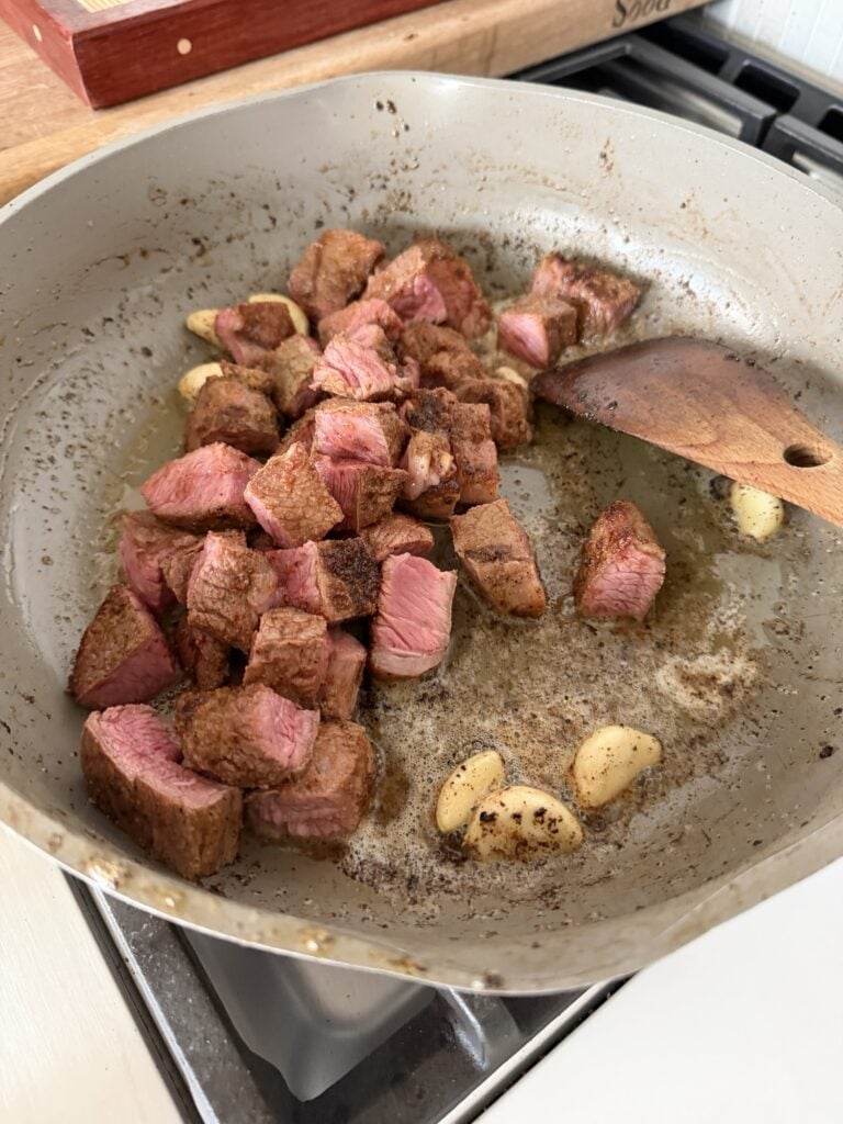 Steak cubes and garlic cooking in butter in the pan