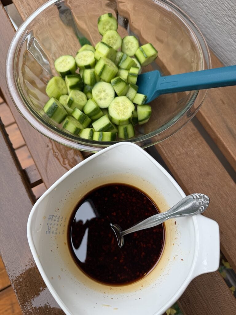 A bowl of sliced cucumbers next to a bowl of dressing
