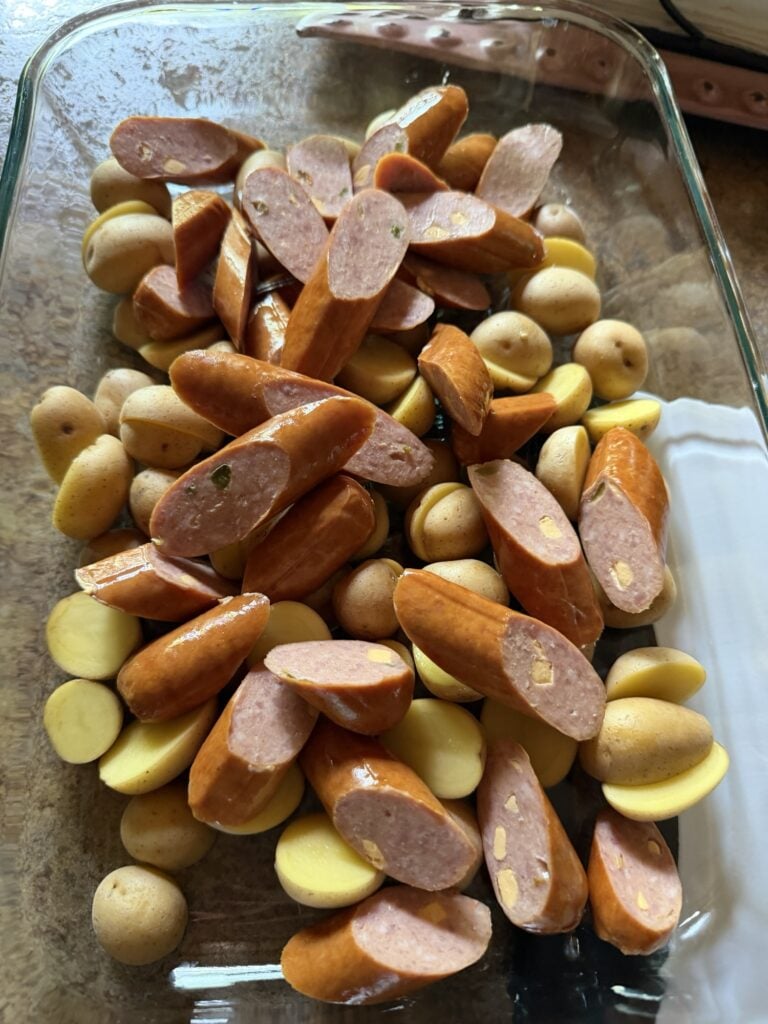 The sausage and potatoes in the baking dish before being baked