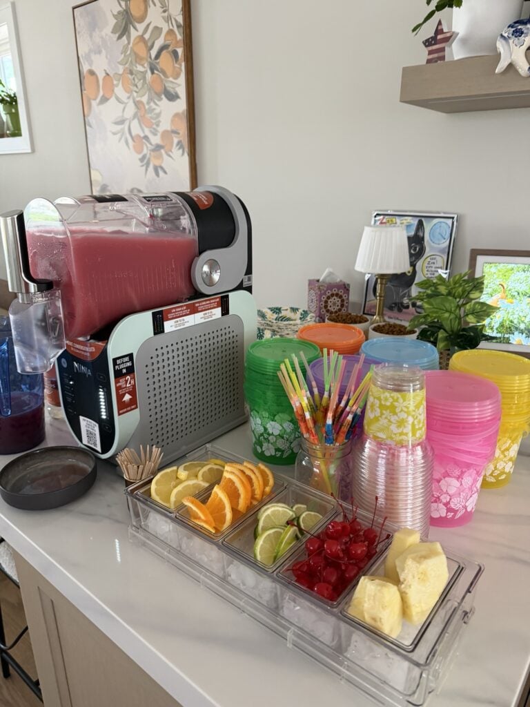 The slush in the Ninja SLUSHi machine next to cups, straws, and fruit toppings