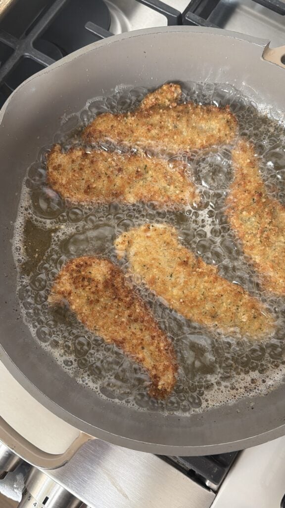 The chicken strips frying in the pan