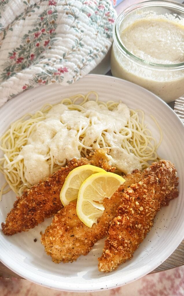 The chicken tenders on a plate next to the pasta topped with the sauce