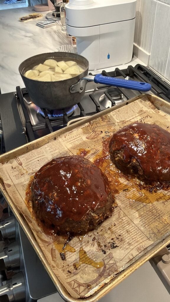Two meatloafs next to a pot of boiling potatoes