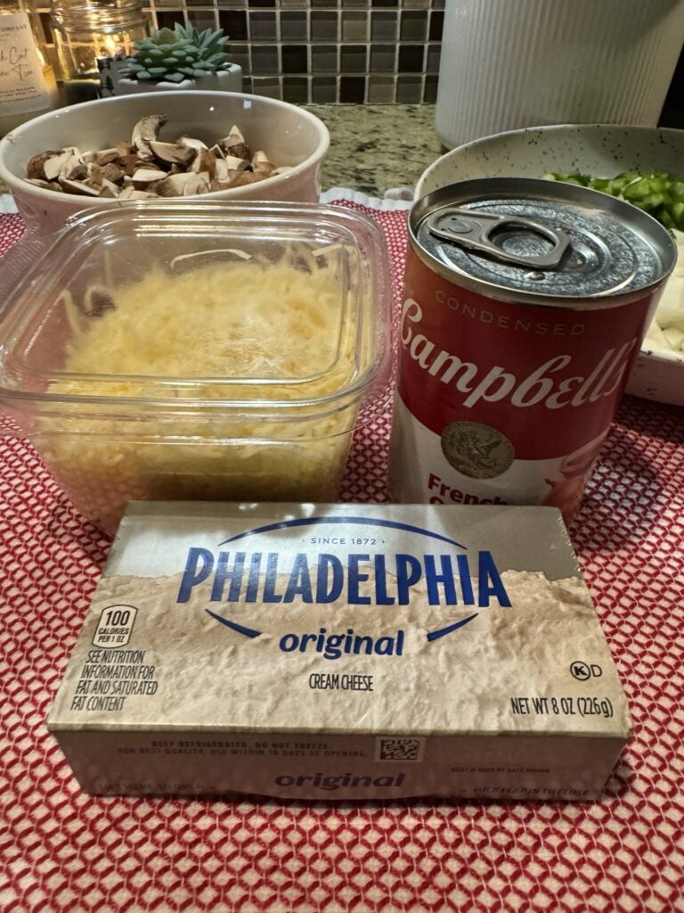 Ingredients for easy Philly Cheesesteak Pasta on the counter including cheese, cream cheese, and a can of soup