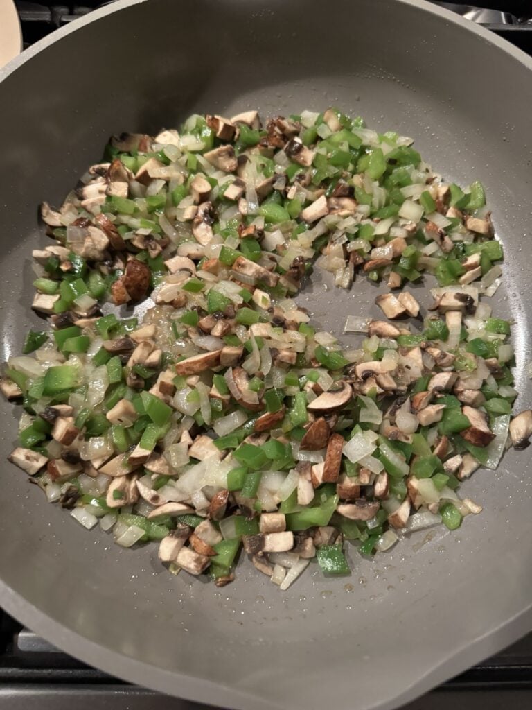 Green peppers onions, and mushrooms sautéing in the pan
