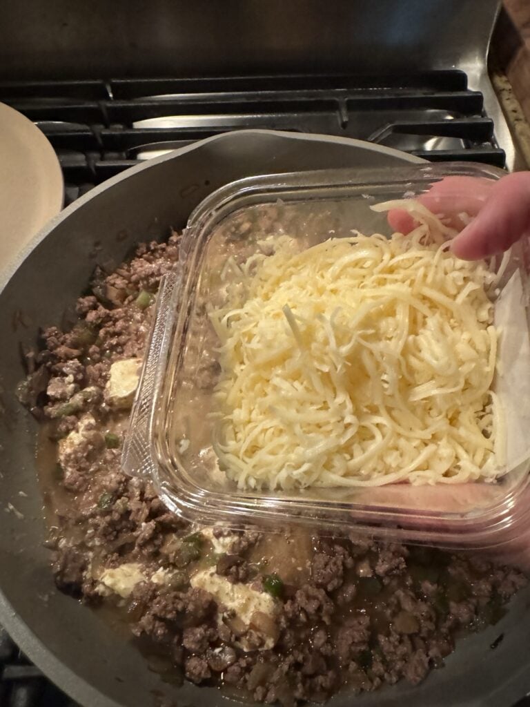 A package of shredded cheese over the beef cooking in the pan