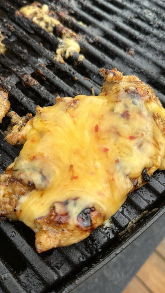 The cheese melting on the chicken on the grill