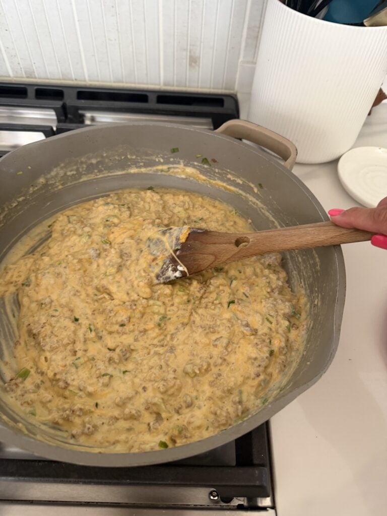 The creamy mixture in the pan being stirred with a wooden spoon