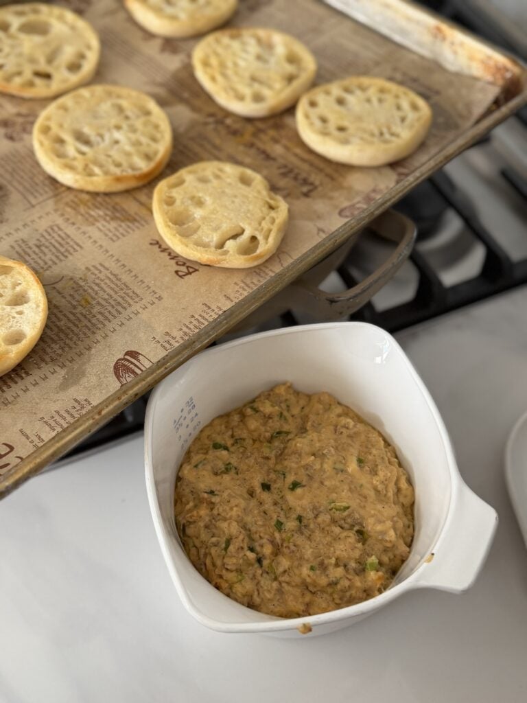 The sausage cheese topping next to the English muffins on a baking sheet
