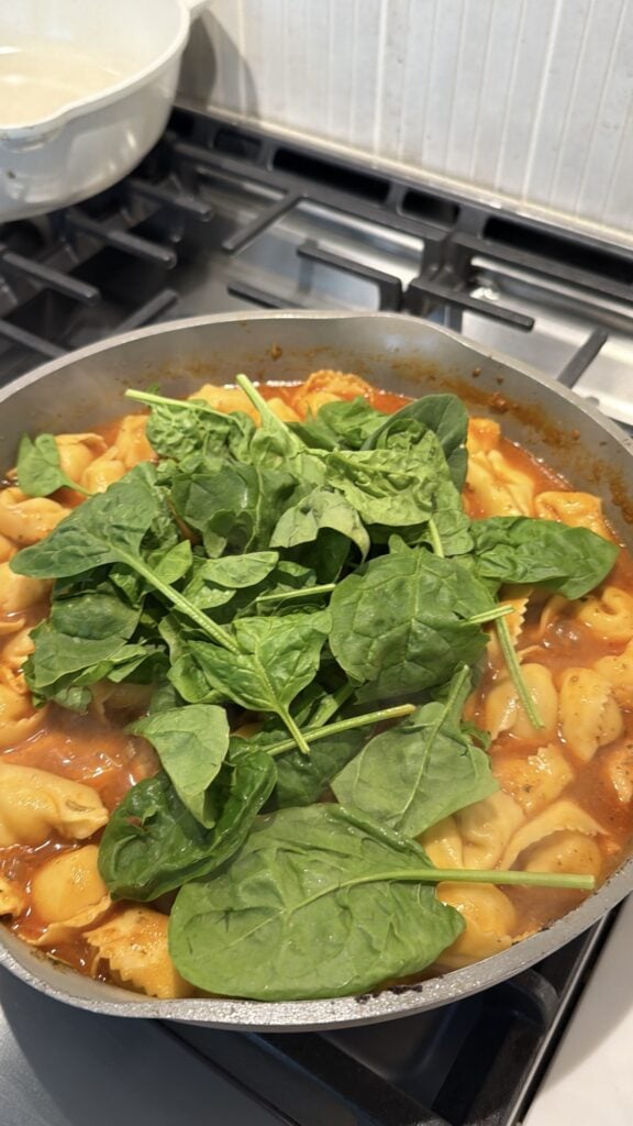Fresh spinach added to the chicken and cheese tortellini skillet in the pan